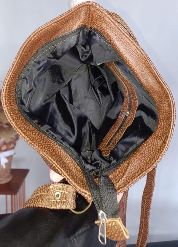Inside view of the Rosy Genuine Leather Handbag by J&S Creations, revealing spacious interior with black lining, zip compartments, and side pockets for organized storage.