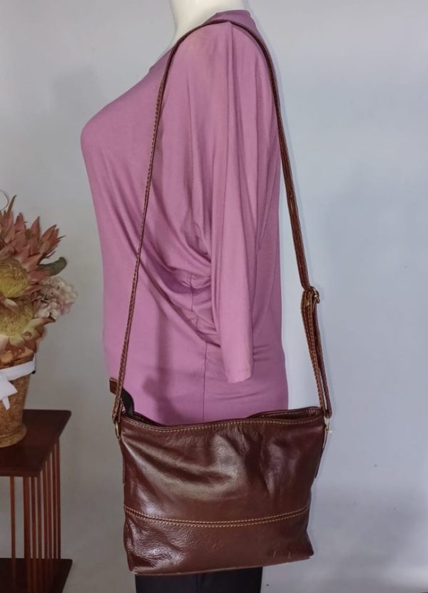 Rosy Genuine Leather Handbag in dark brown by J&S Creations, worn crossbody on mannequin, showcasing comfortable adjustable strap and soft textured finish. Dimensions: 25cm x 22cm.