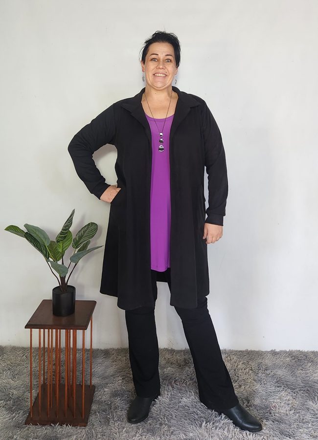 Woman wearing a black Cosy Collar Zelda Cardigan over a purple tunic top and black pants, styled with black boots.